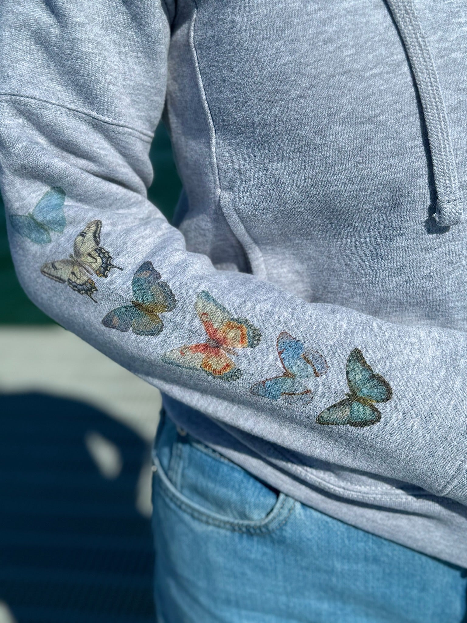 Gray hoodie with watercolor butterflies on the sleeve, worn by a person.