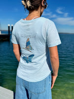 Person wearing a light blue t-shirt with butterfly design by a waterfront
