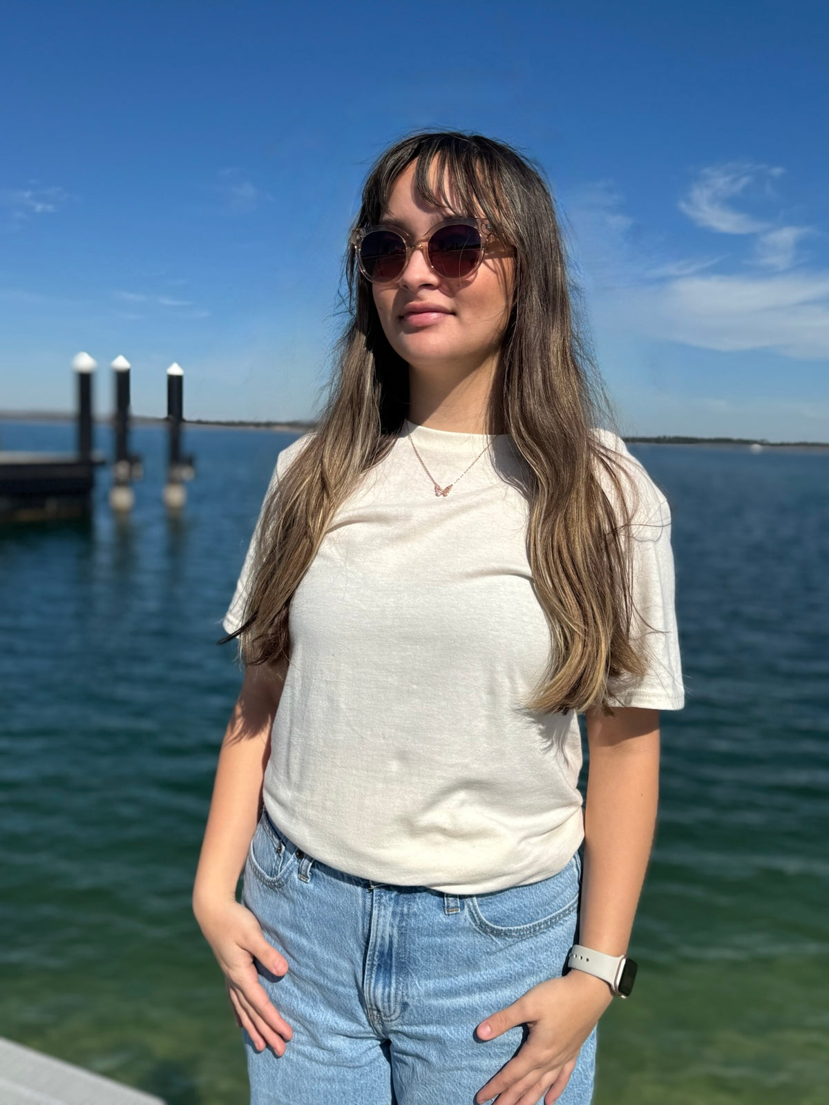 Woman wearing a cream t- shirt  standing by the water with blue sky