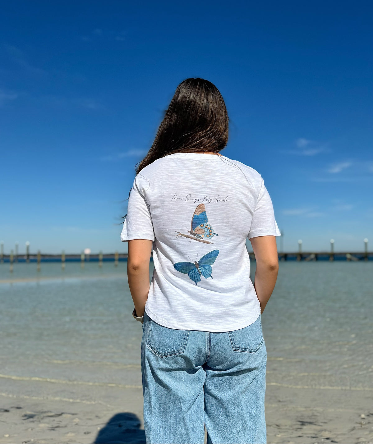 Person wearing a white t-shirt with a Butterfly design on a beach