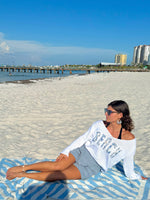 Woman sitting on a beach with a blue sky and ocean in the background