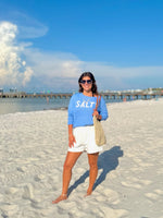 Woman in a blue sweatshirt with 'SALTY on a beach