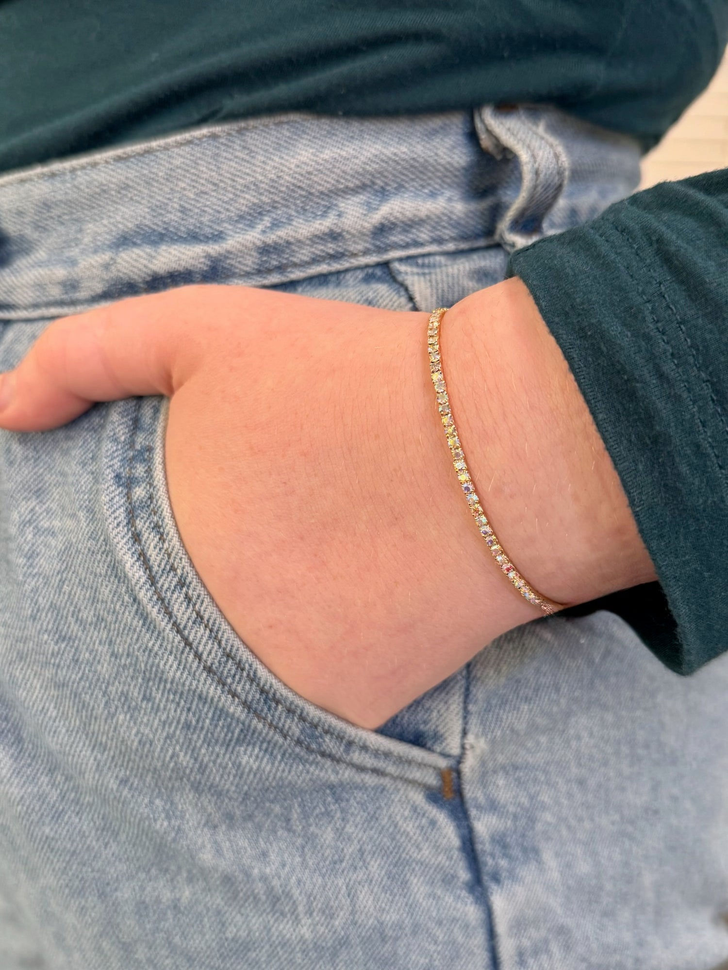 Close-up of a person wearing a gold bracelet on a light blue denim background