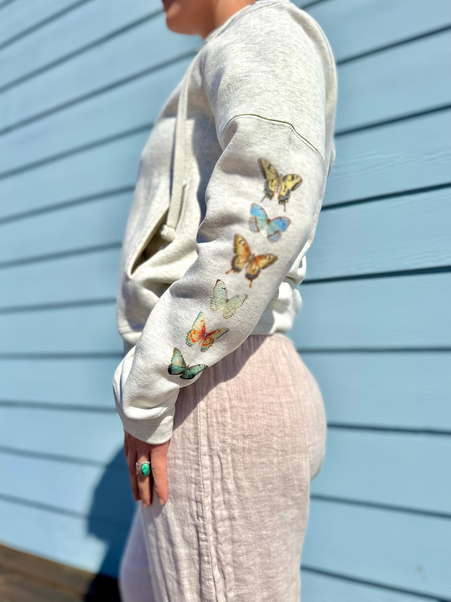 Person wearing a light gray sweatshirt with colorful butterfly designs against a blue wall.