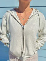 Person wearing a light gray hoodie with butterflies on sleeve  blue background