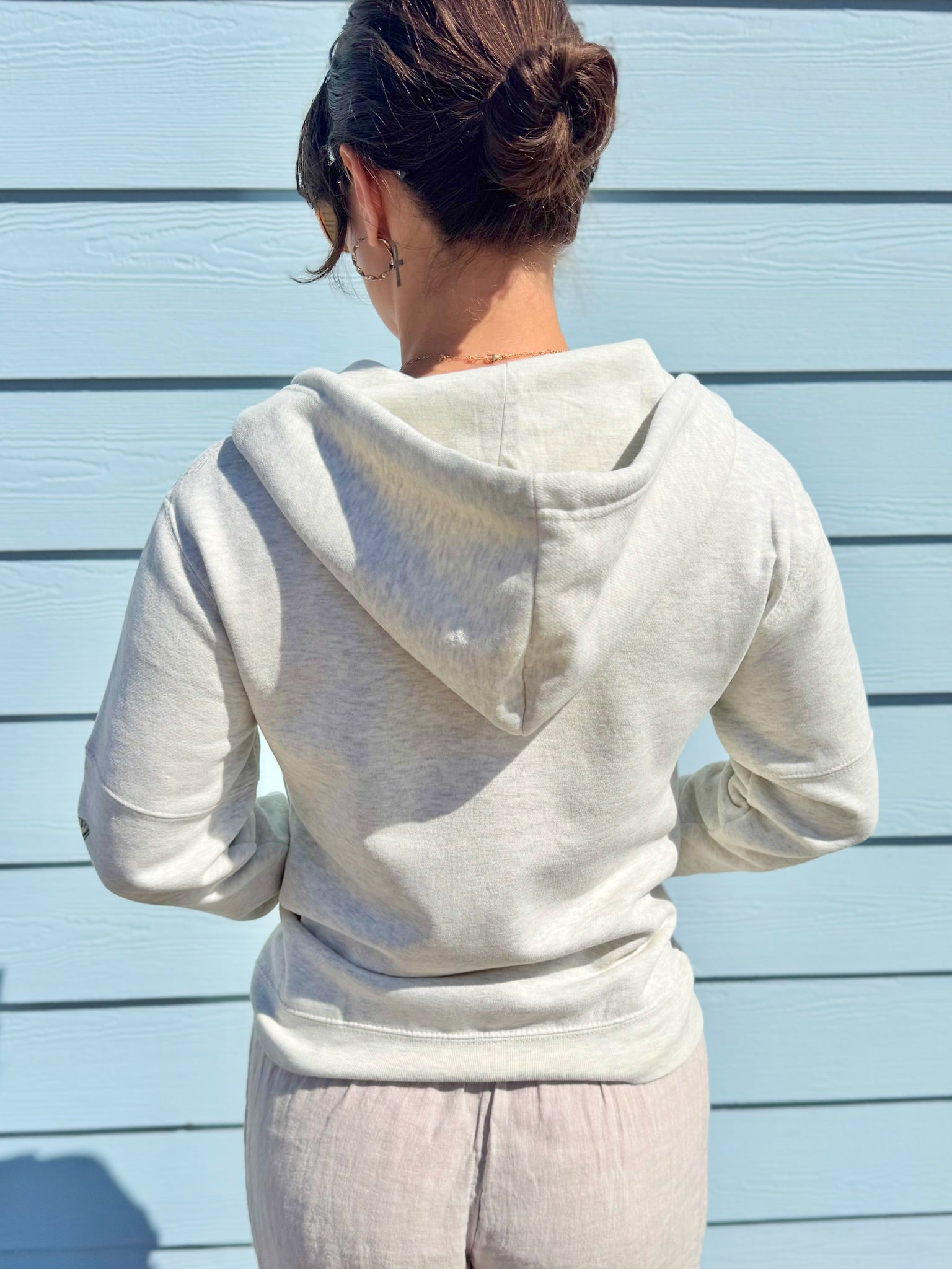 Person wearing a light gray hoodie and pants against a light blue wall.