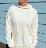 White hoodie with colorful designs on sleeves against a blue wall