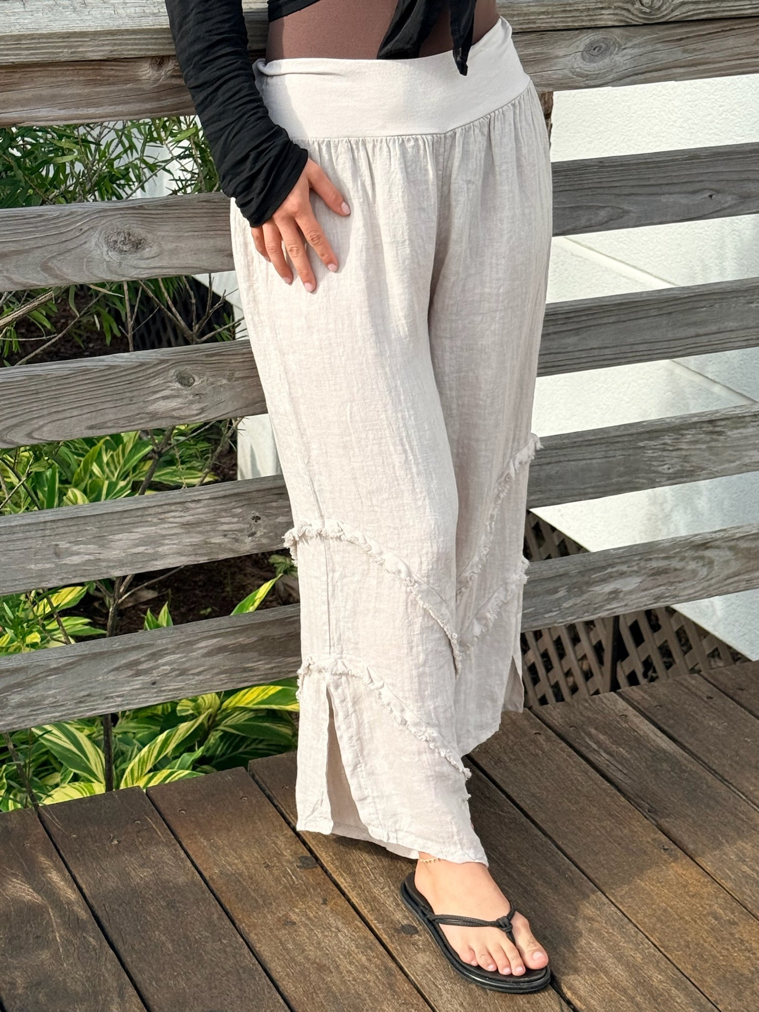 Side angle of neutral linen wide-leg pants featuring diagonal frayed trim and a relaxed, flowy fit paired with a casual black top.