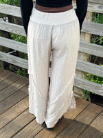 Back view of beige wide-leg linen pants showing soft textured fabric, tiered frayed seams, and a comfortable elastic-style waistband.