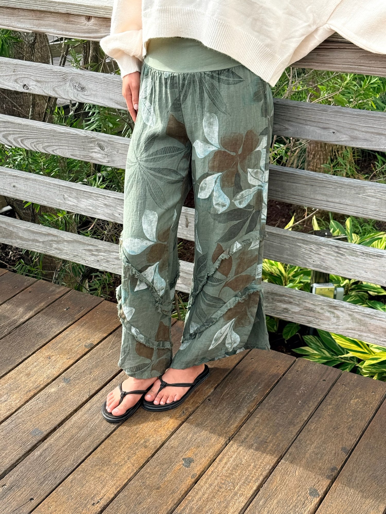 Green floral linen pants featuring frayed seams and a comfortable pull-on waistband, worn with a cream top and black sandals.