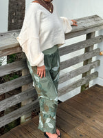 Printed green linen pants with a relaxed wide-leg silhouette, paired with a cream sweater for a cozy, casual look.