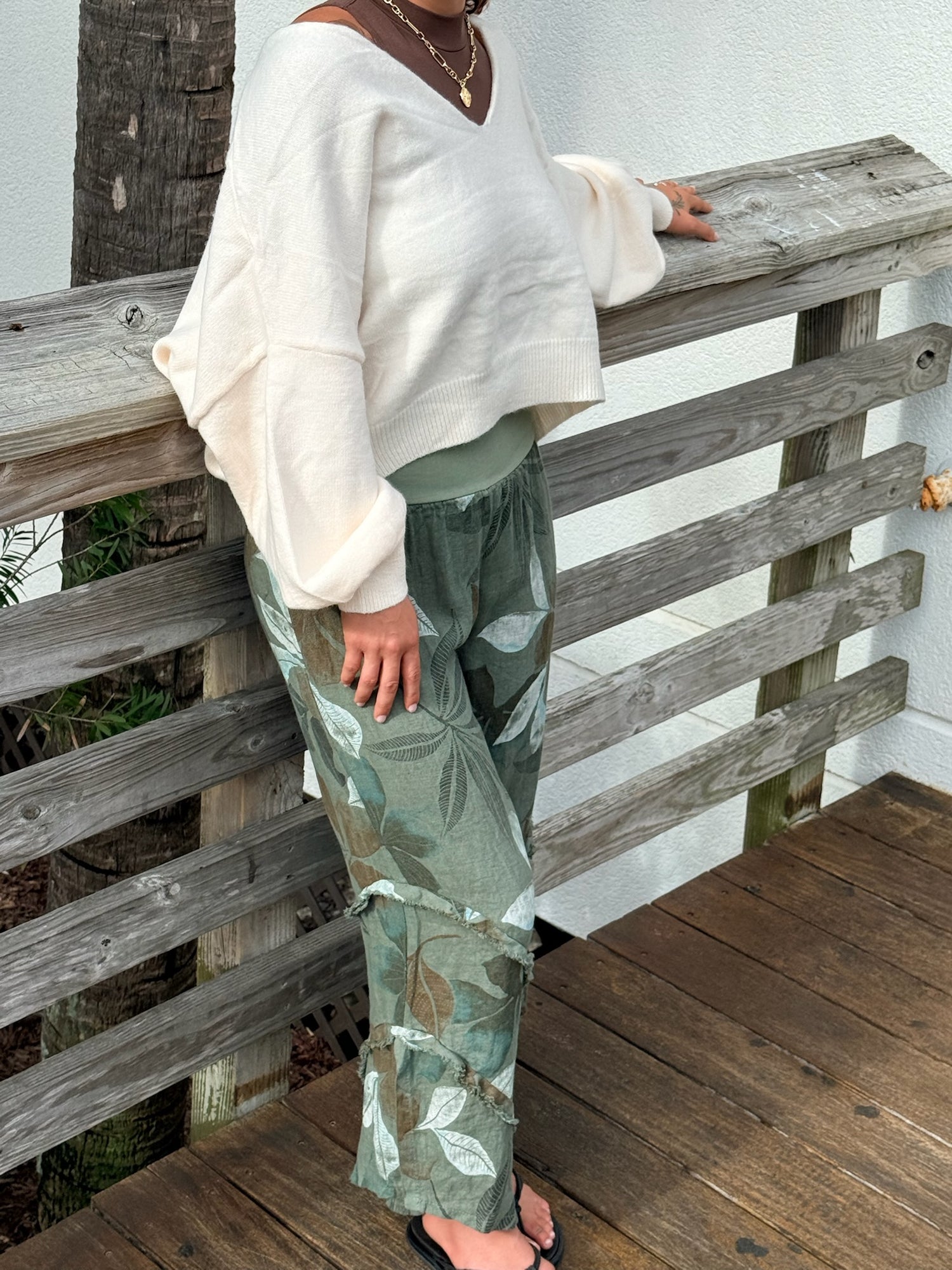 Printed green linen pants with a relaxed wide-leg silhouette, paired with a cream sweater for a cozy, casual look.