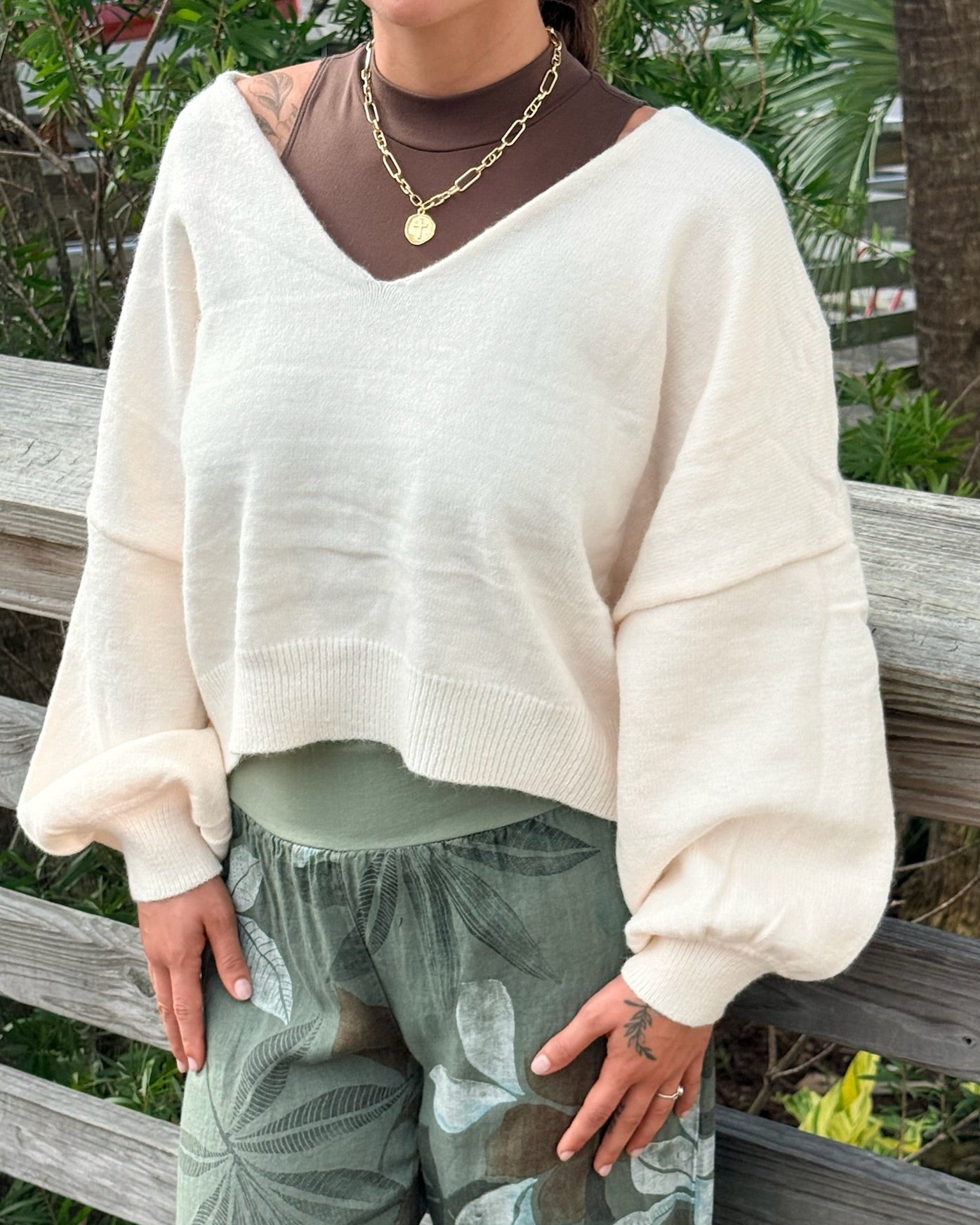 Person wearing a white sweater and green patterned pants sitting on a wooden bench.