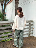 Green floral printed linen pants with wide legs and frayed seam details, styled with an ivory sweater and sandals.