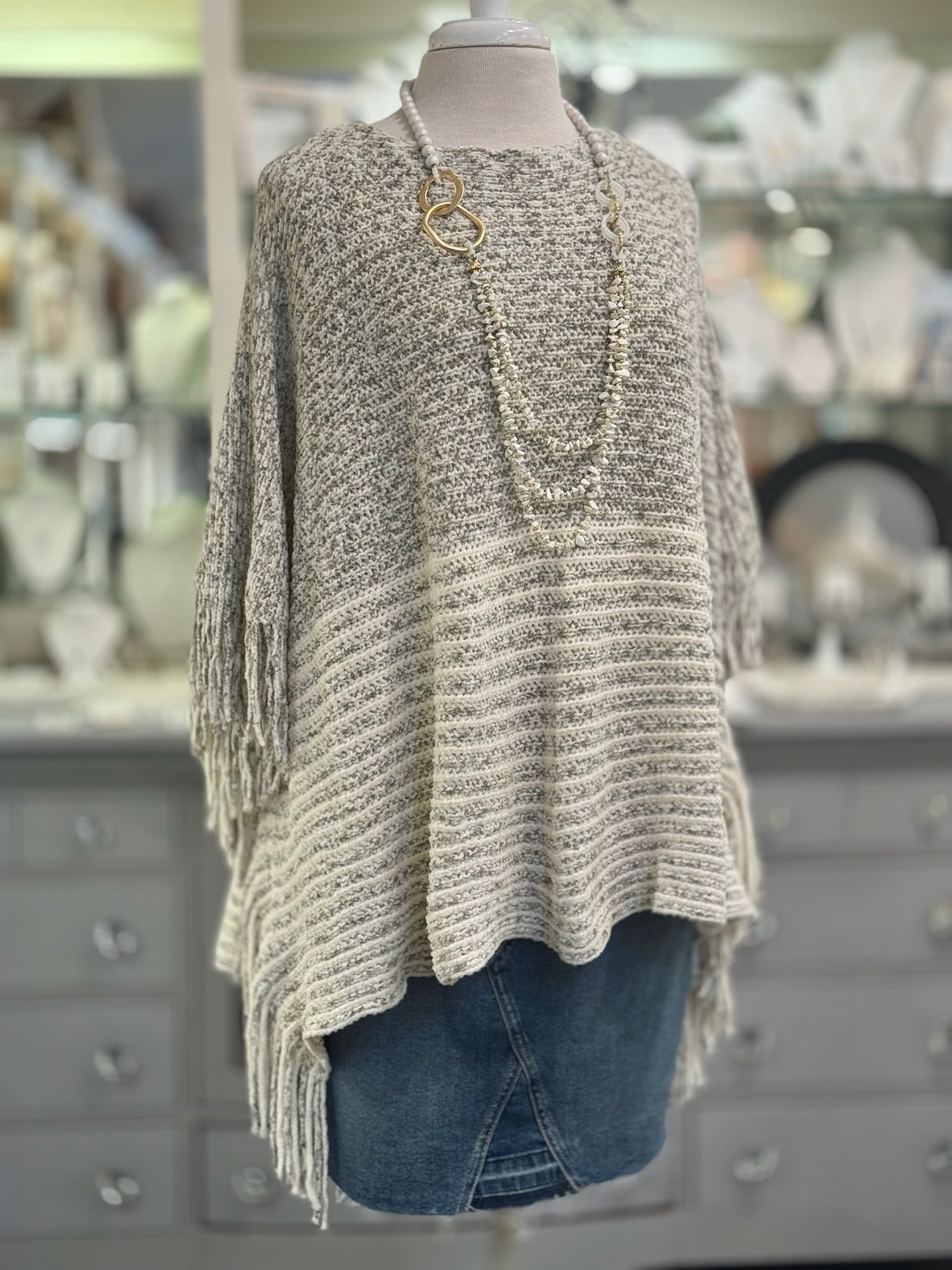 Knitted poncho on a mannequin in front of a store display.