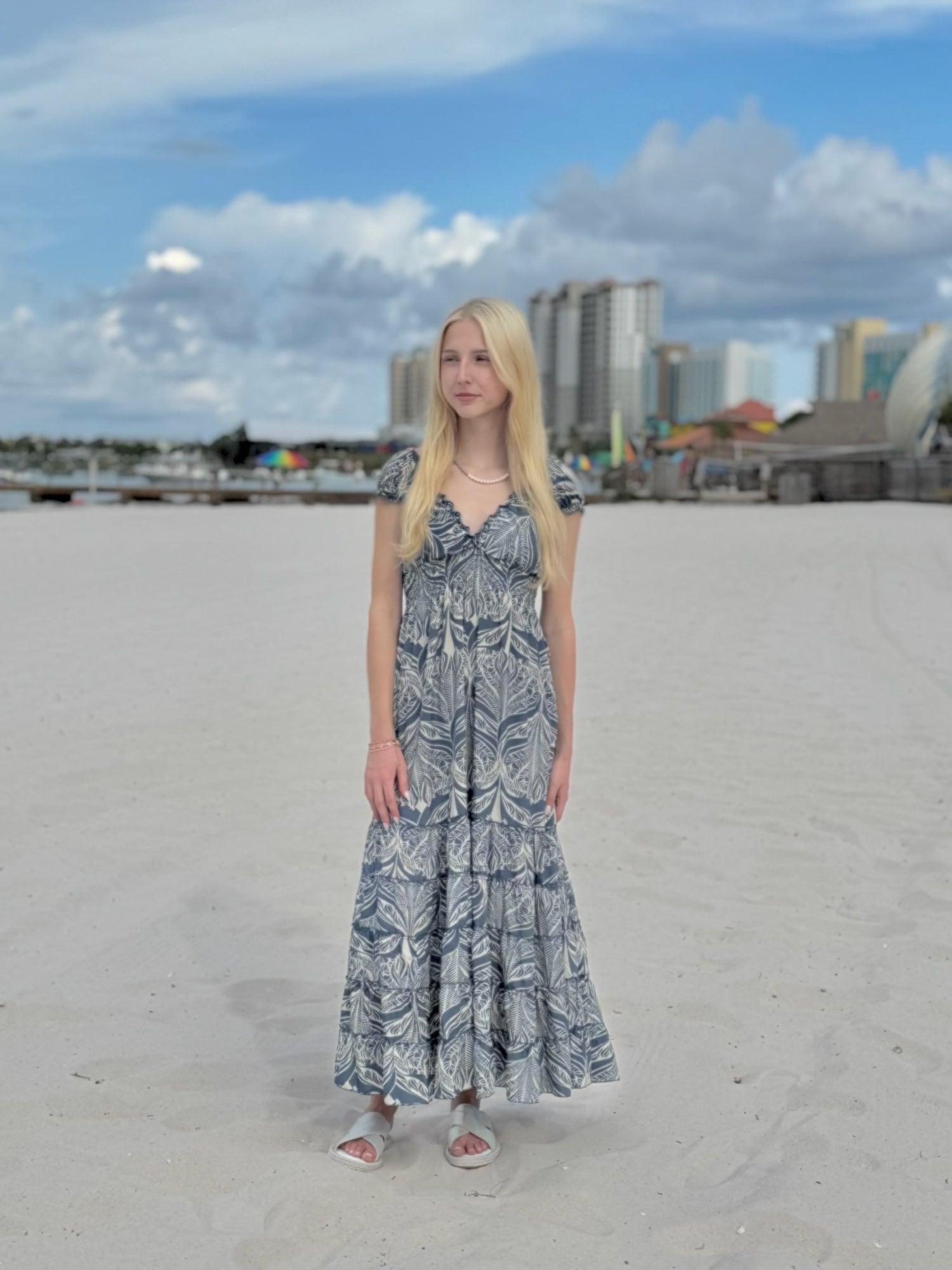 Woman in a long dress standing on a sandy beach with buildings in the background