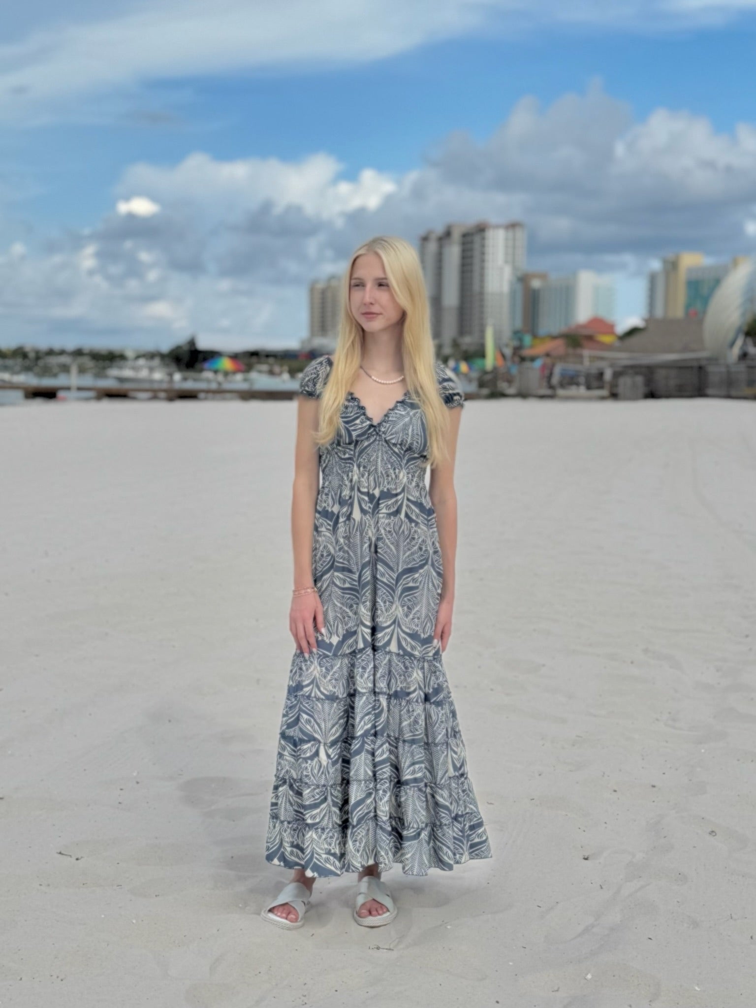 Woman in a long dress standing on a sandy beach with buildings in the background