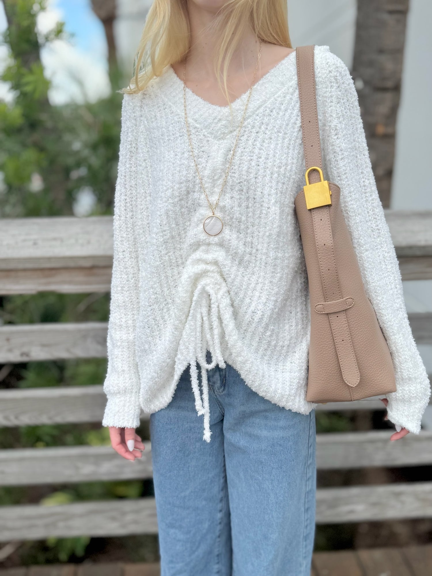Person wearing a white knitted sweater and blue jeans, holding a beige handbag.