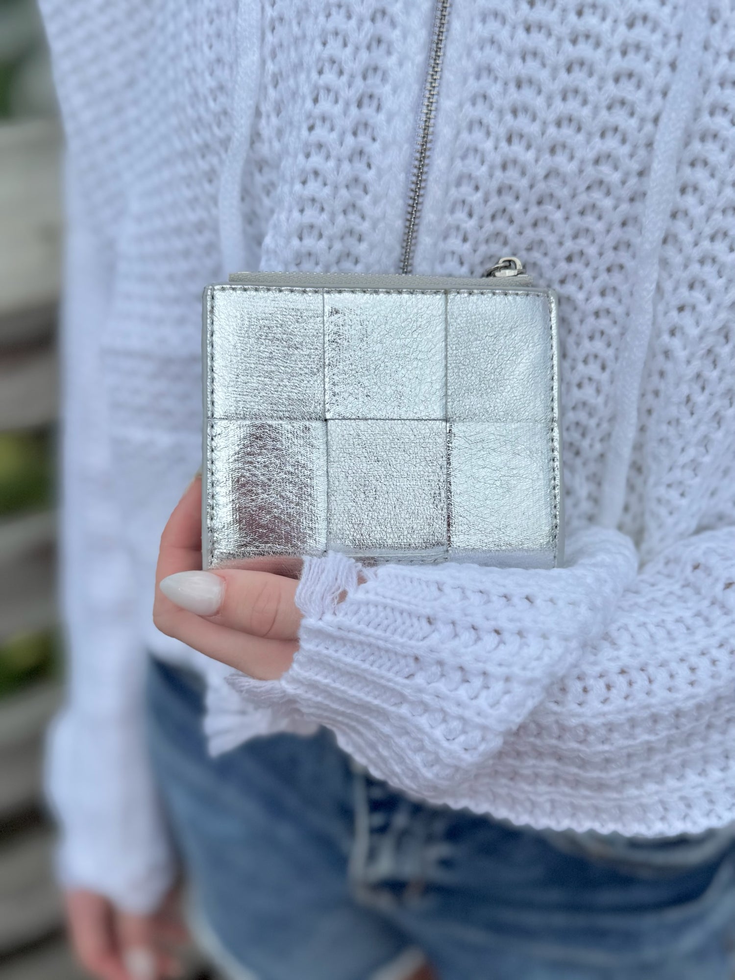 Silver quilted wallet held by a person wearing a white textured sweater.