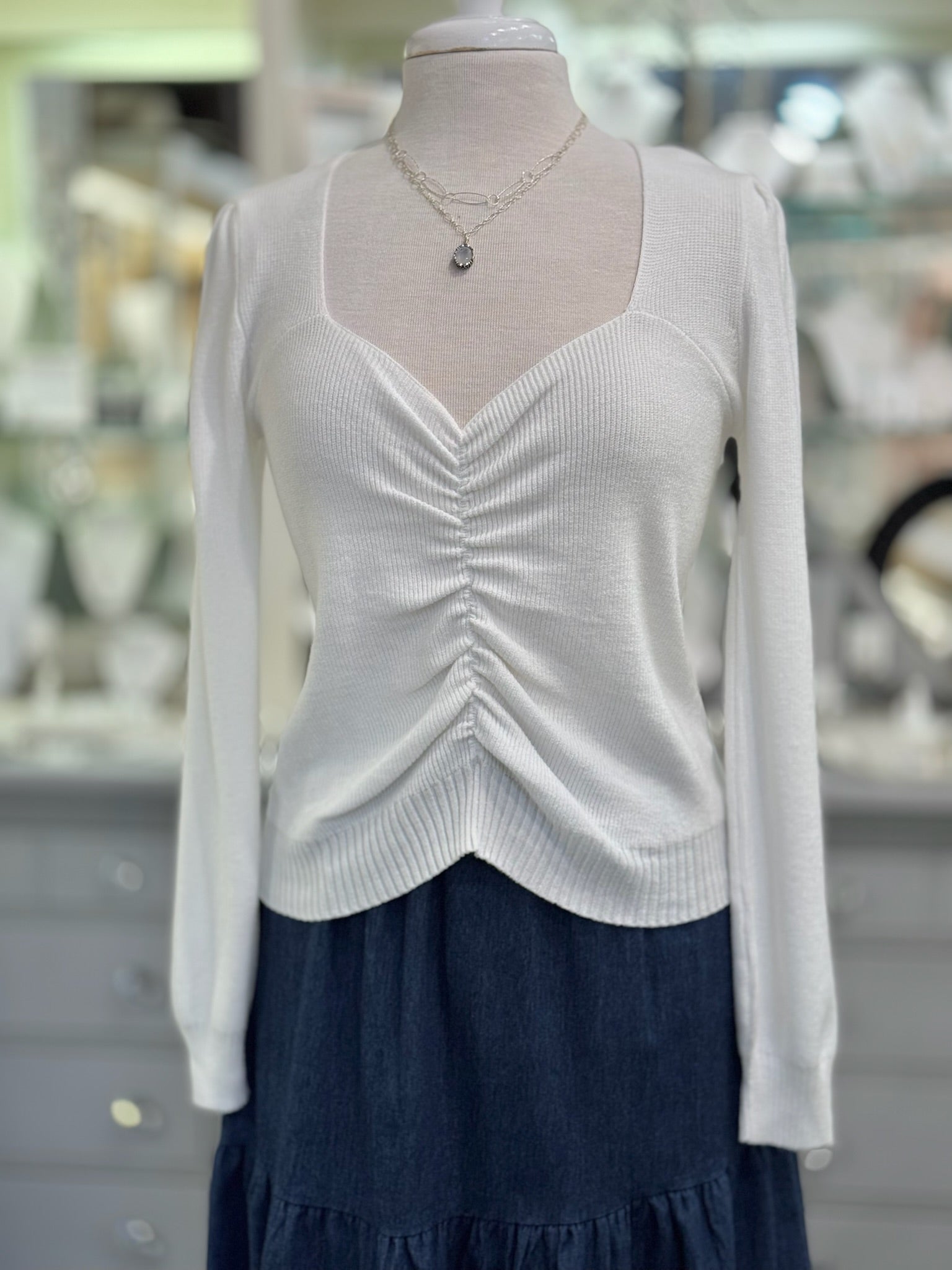 White long-sleeve top on a mannequin with a blurred store background