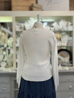 White sweater on a mannequin in front of a store display with shelves and products.