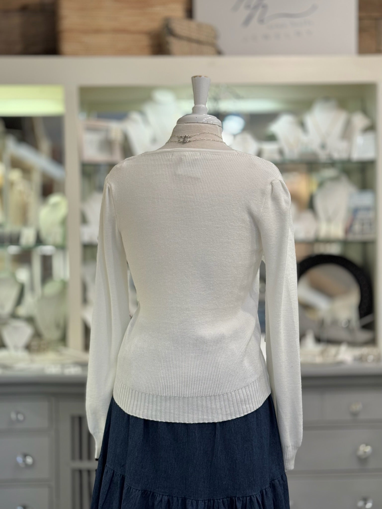 White sweater on a mannequin in front of a store display with shelves and products.