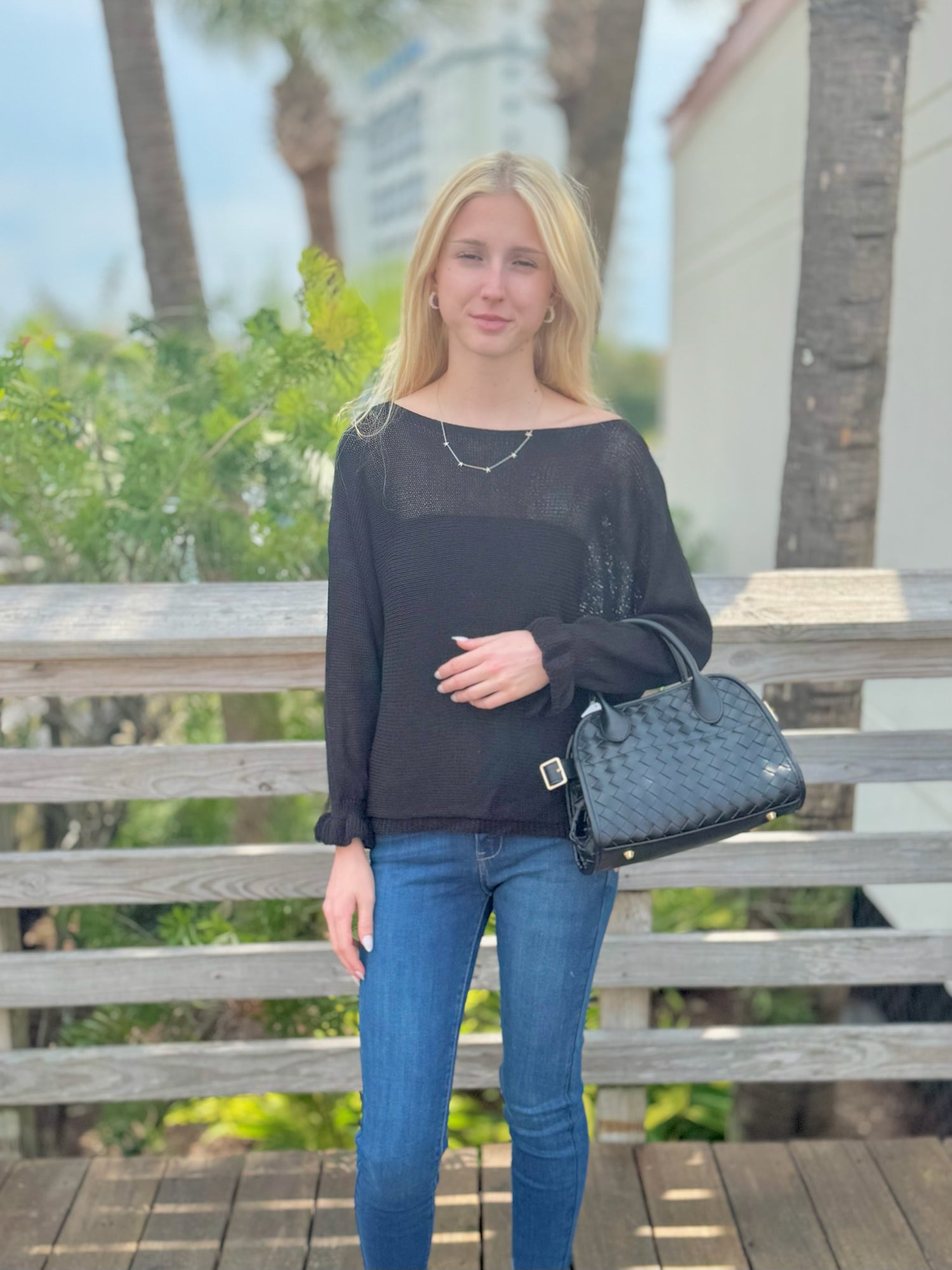 Woman holding a black handbag outdoors with blurred background