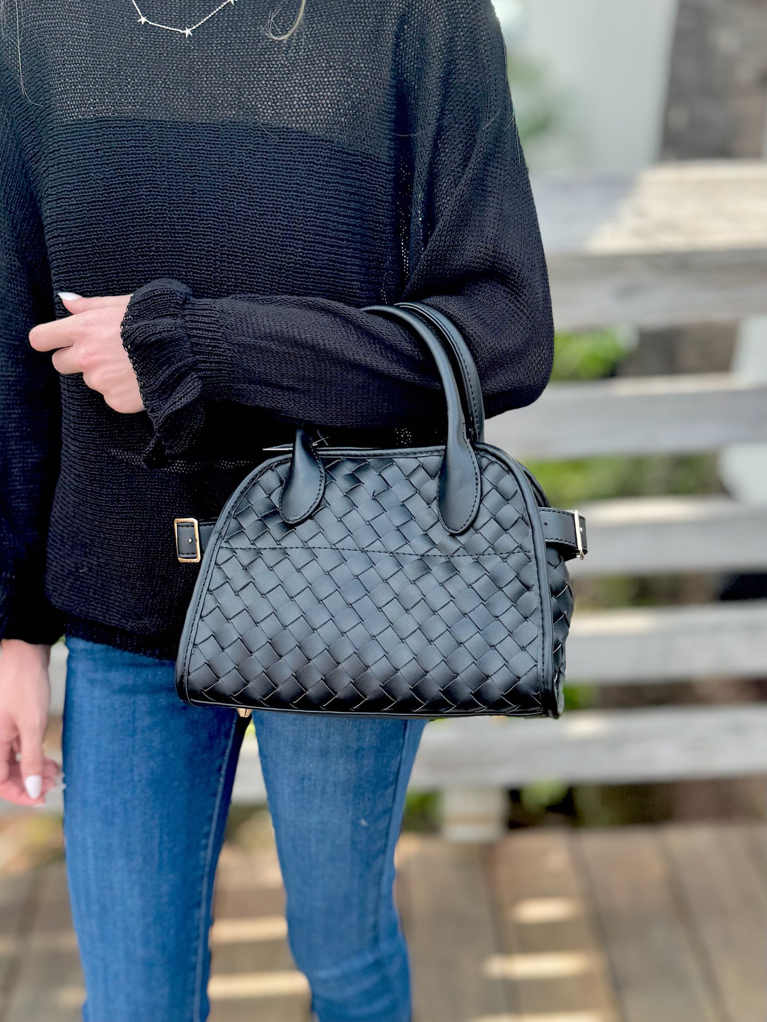 Person holding a black woven handbag outdoors