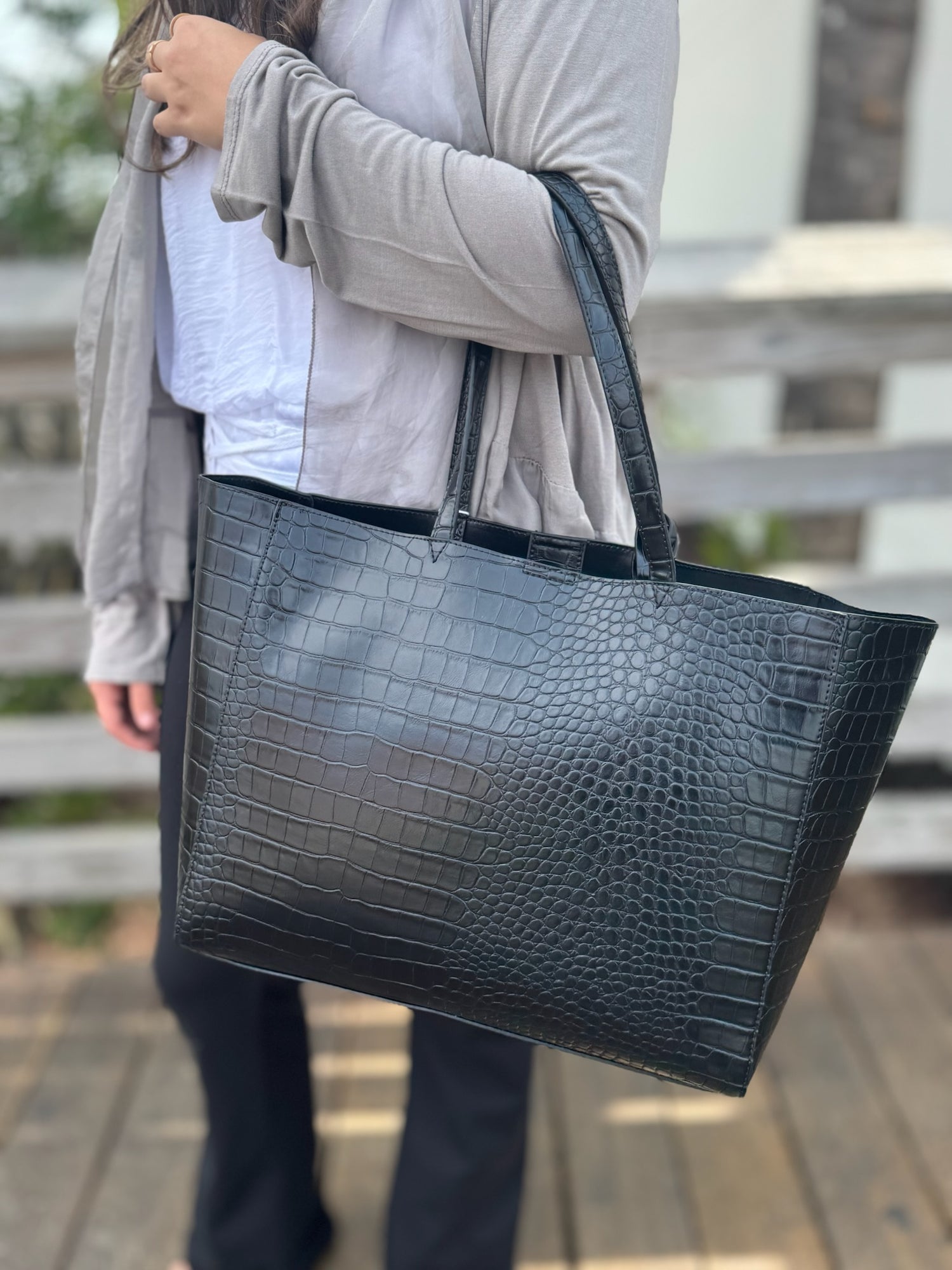 Person holding a black textured tote bag outdoors.
