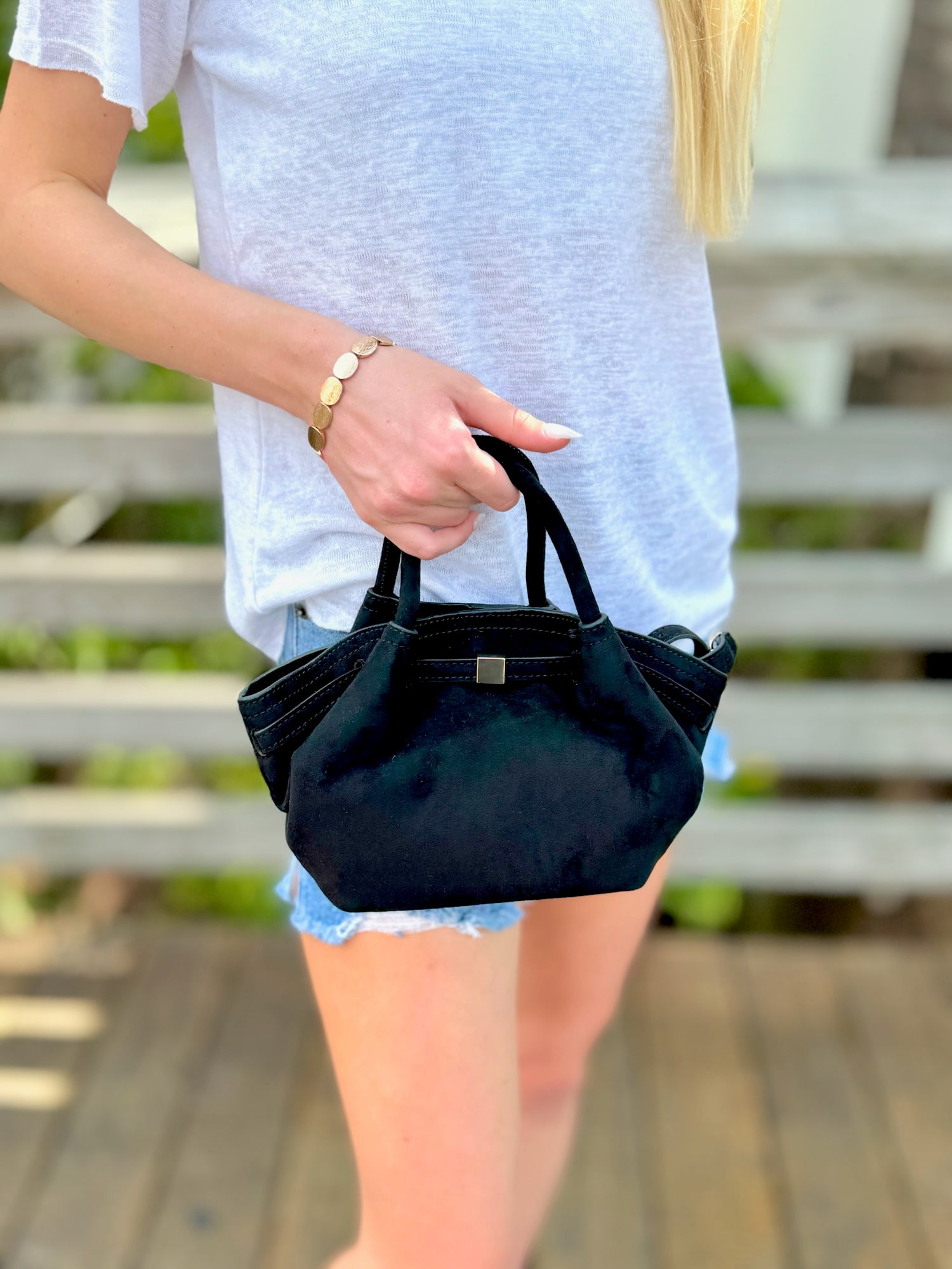 Person holding a black handbag outdoors on a wooden deck