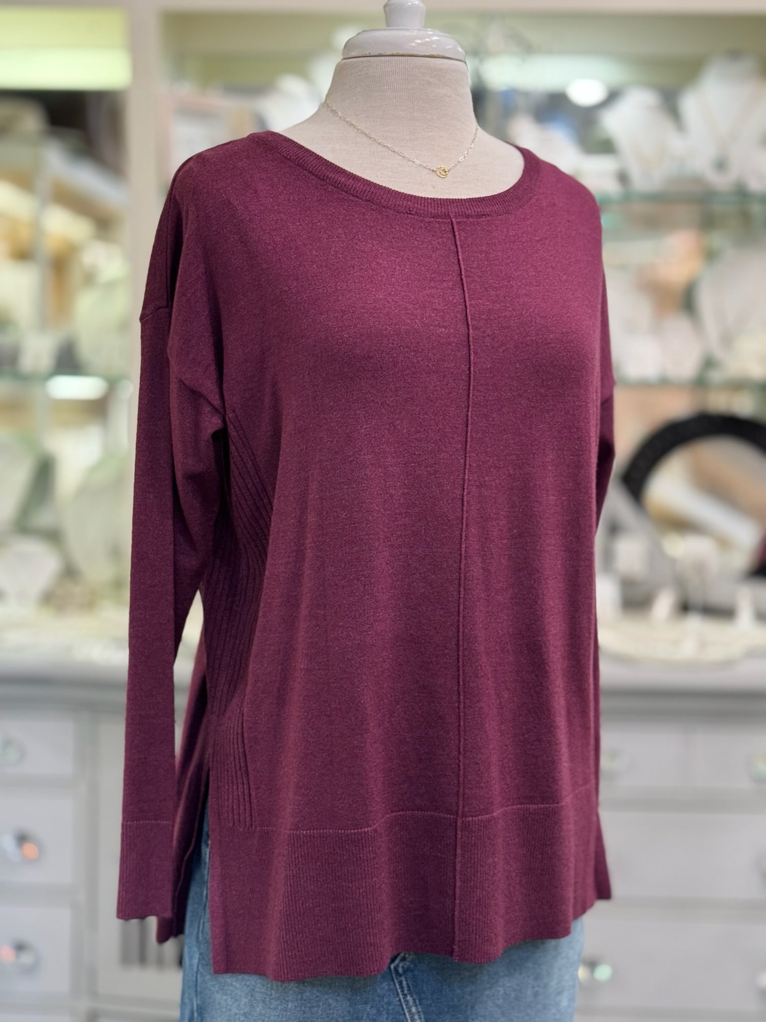 Maroon long-sleeve top on a mannequin with a blurred store background