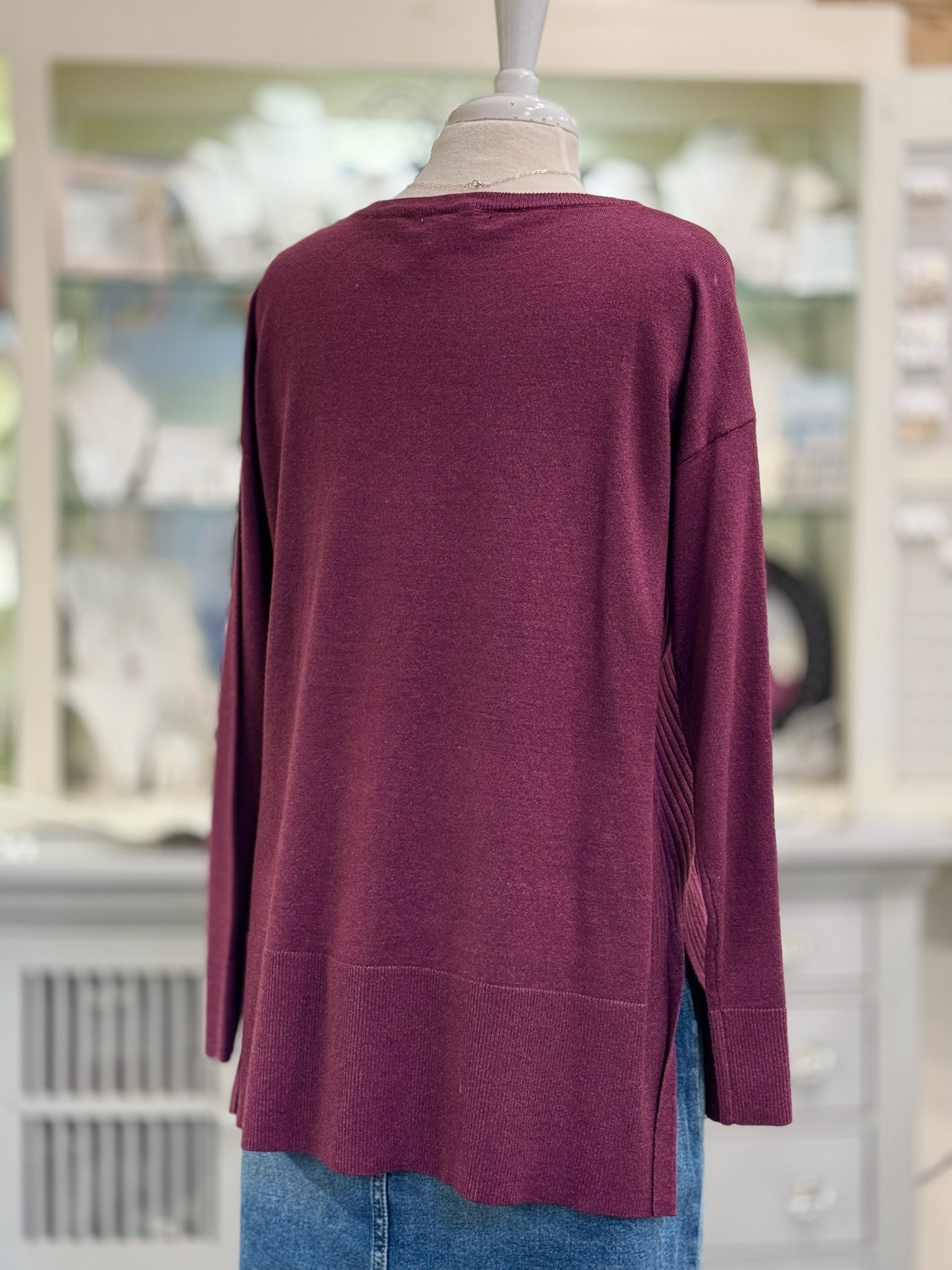 Maroon sweater on a mannequin with a blurred indoor background