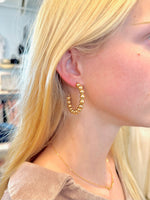 Close-up of a woman wearing gold beaded hoop earrings, styled with straight blonde hair and a delicate gold chain necklace.
