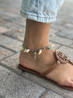 Shell and quartz charm anklet worn around ankle with sandals and denim