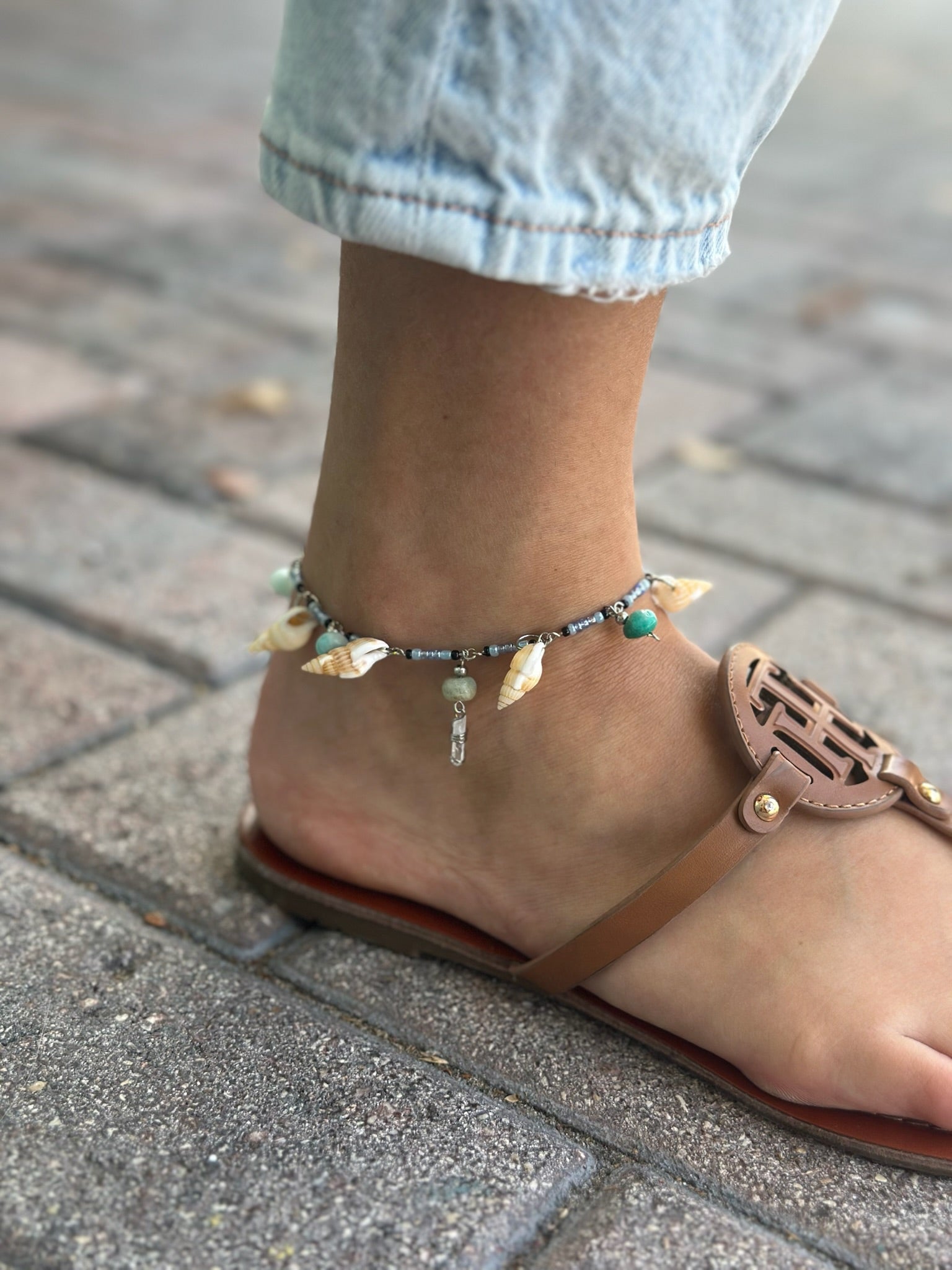 Shell and quartz charm anklet worn around ankle with sandals and denim
