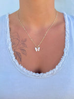 Gold necklace with a butterfly pendant worn by a person against a light blue background