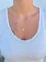 Person wearing a gold starfish necklace on a white top with a blurred background