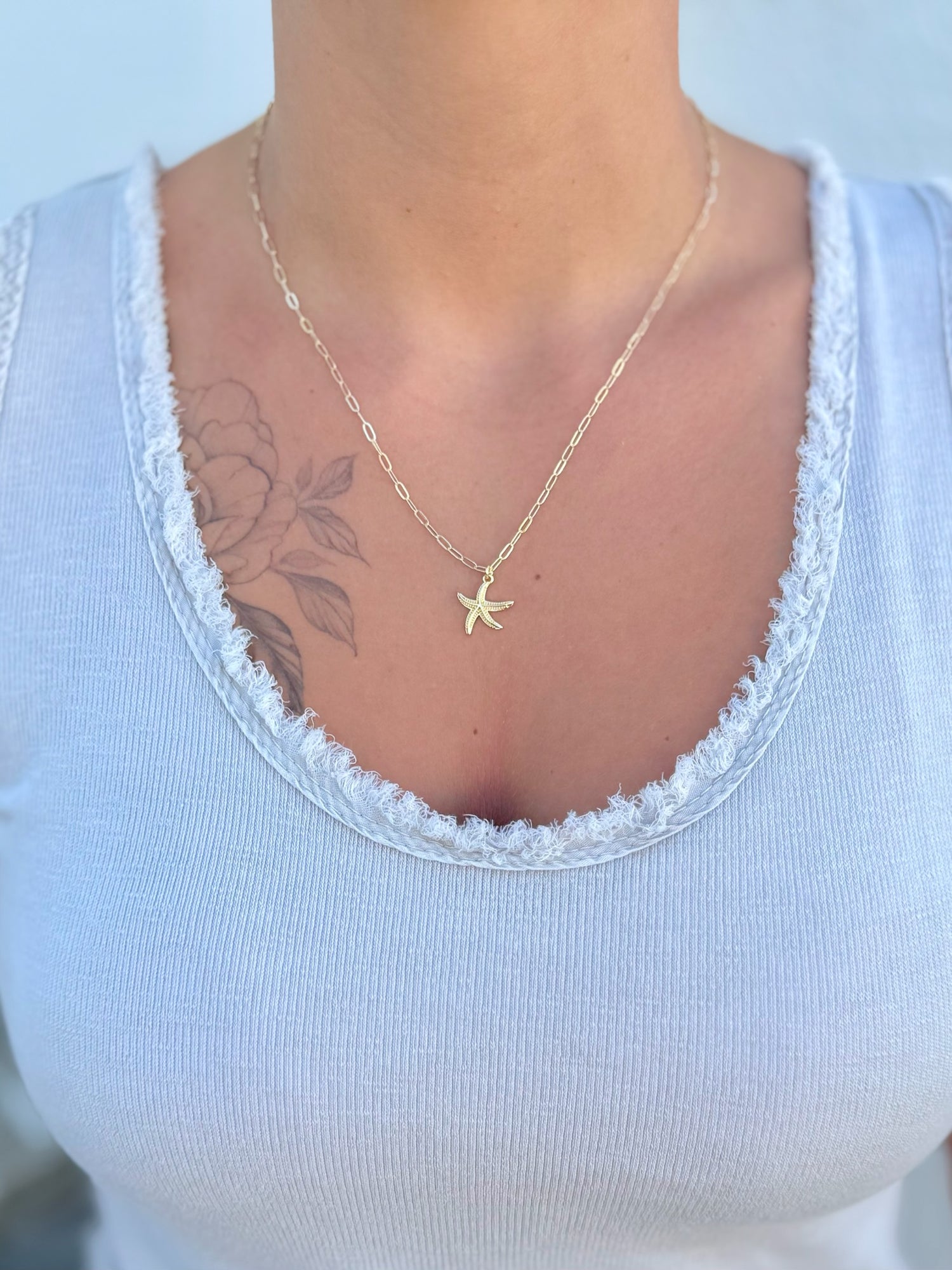 Person wearing a gold starfish necklace on a white top with a blurred background