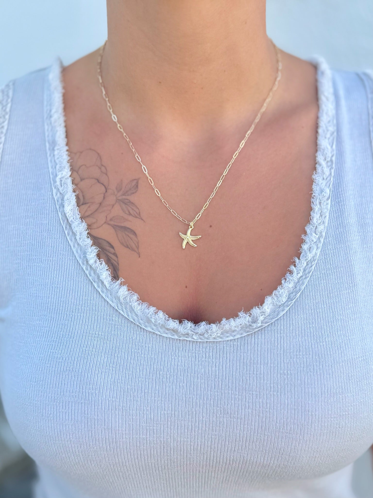 Person wearing a gold starfish necklace on a white top with a blurred background