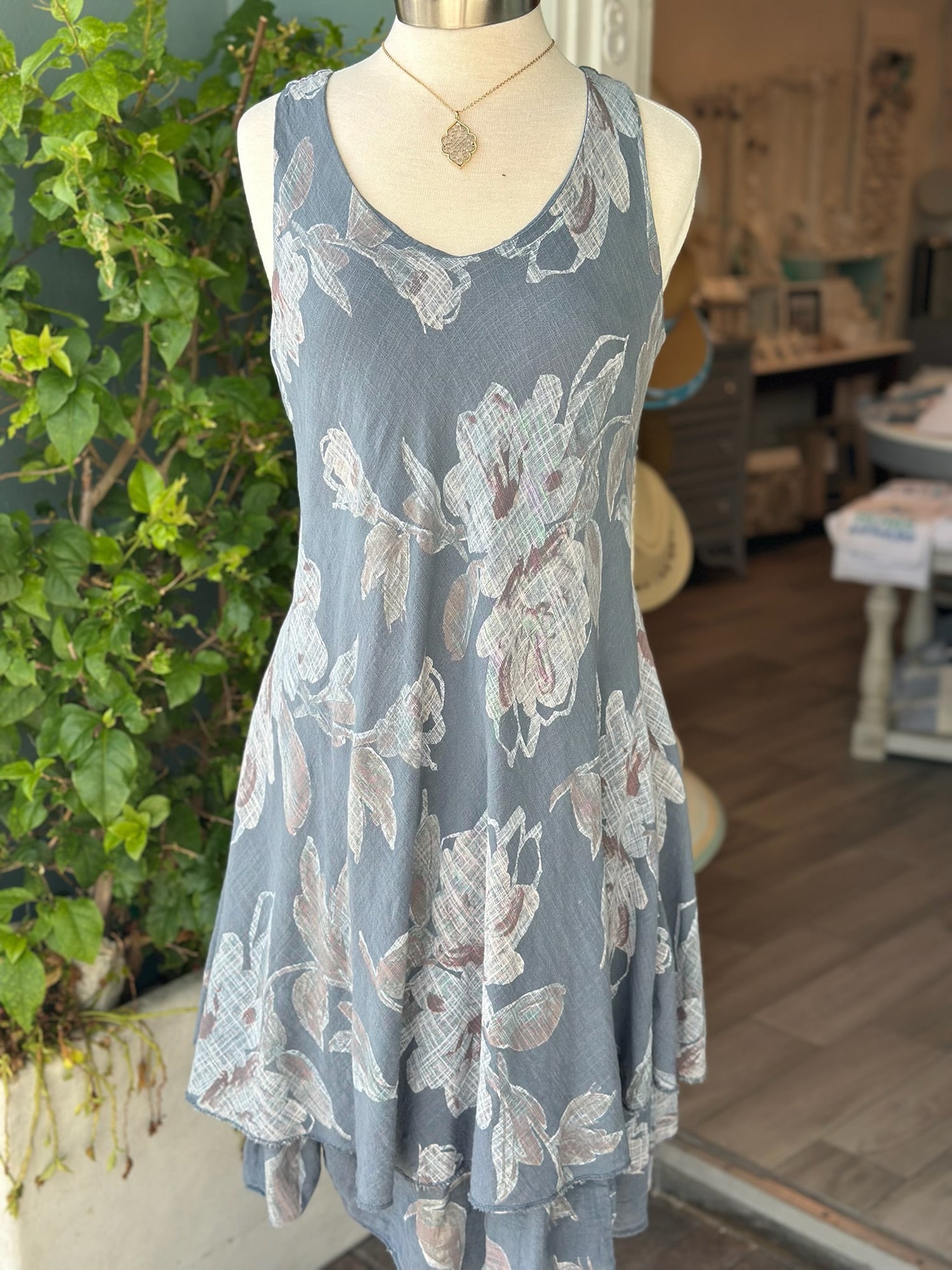 Sleeveless floral Nora Dress in slate blue with handkerchief hem, displayed on mannequin outside Ardor Boutique