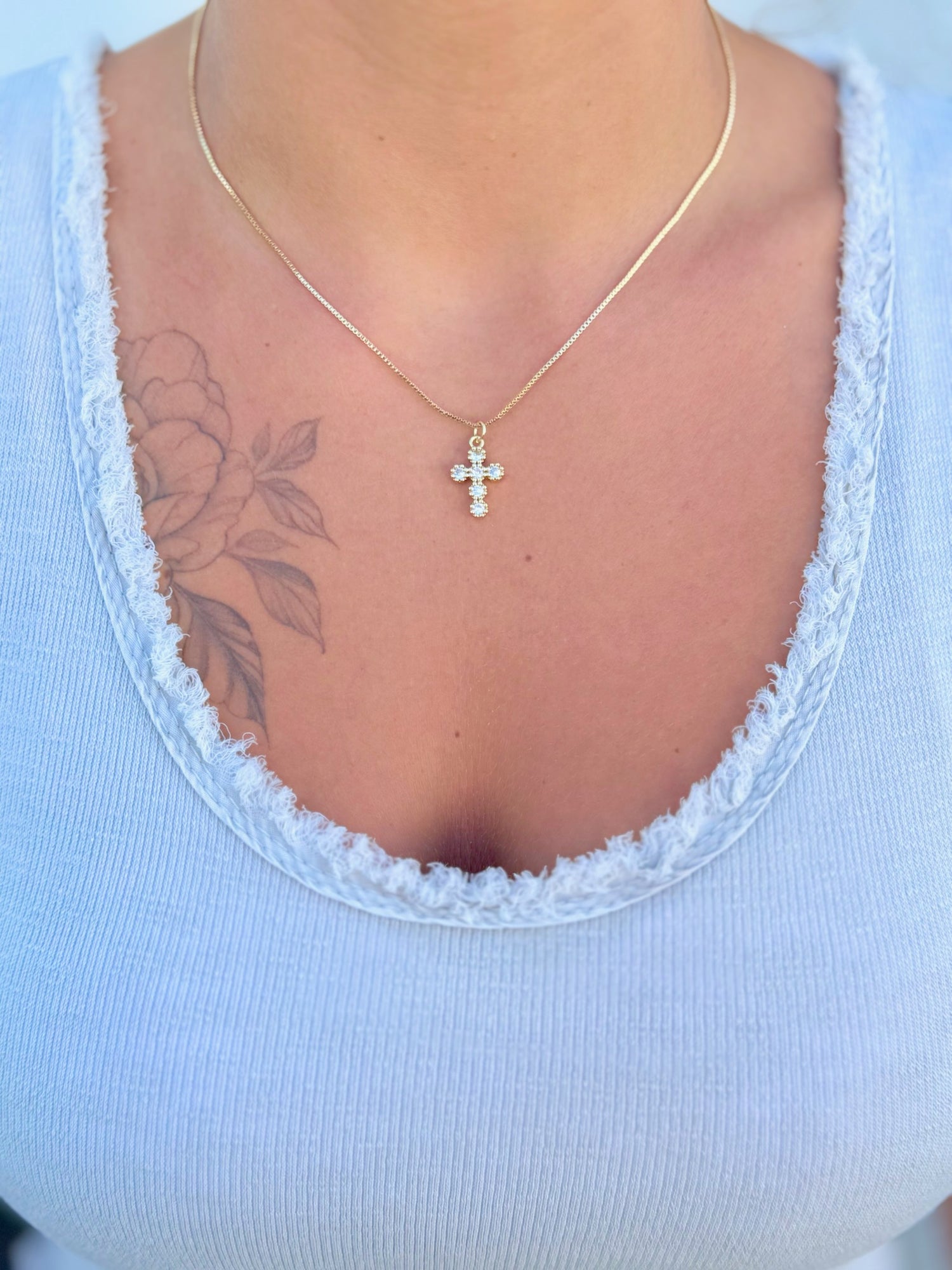 Gold cross necklace with clear stones being worn 