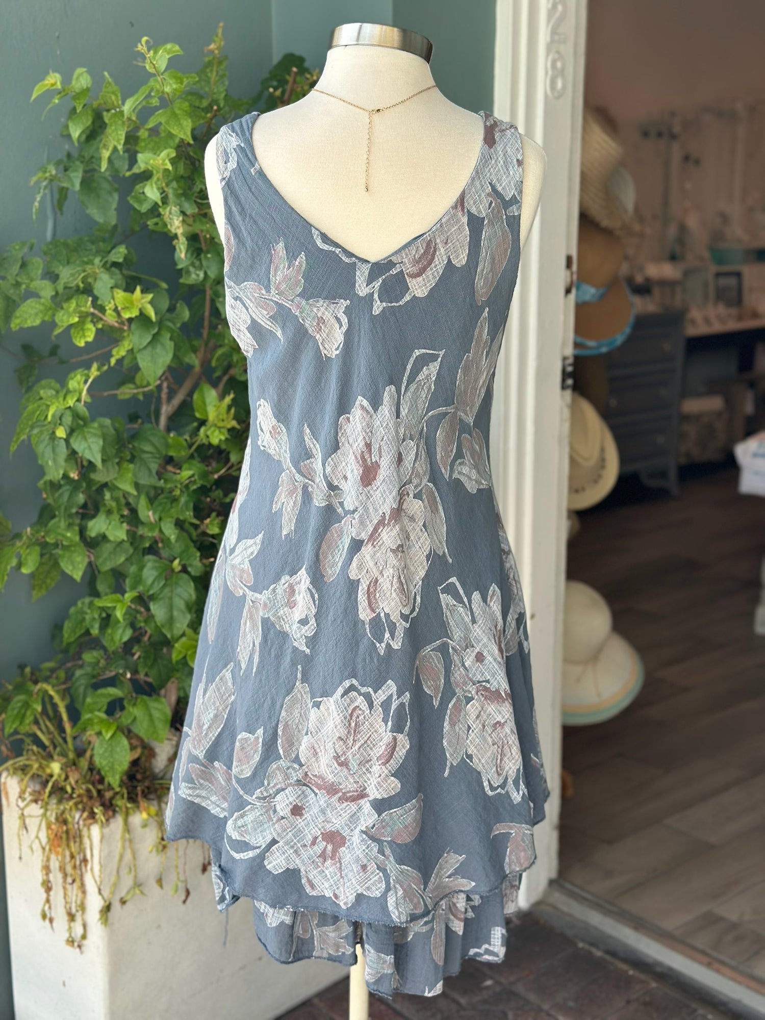 Sleeveless floral Nora Dress in slate blue with handkerchief hem, displayed on mannequin outside Ardor Boutique