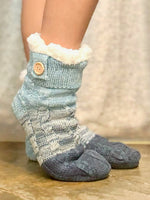 Pair of gray and white patterned socks with a button on a wooden floor.