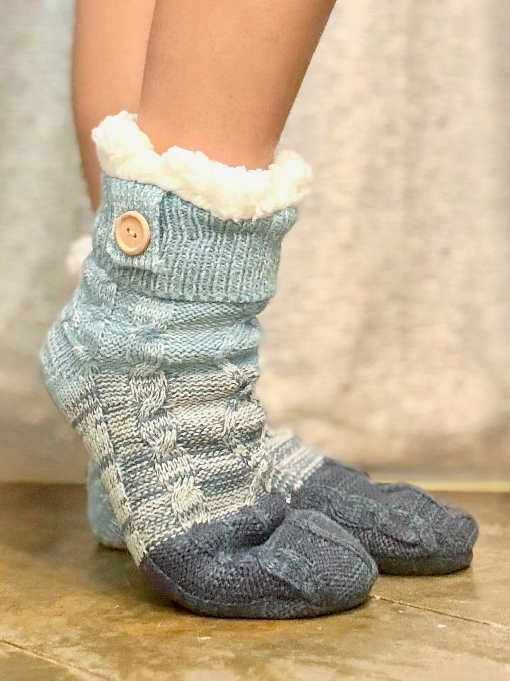 Pair of gray and white patterned socks with a button on a wooden floor.