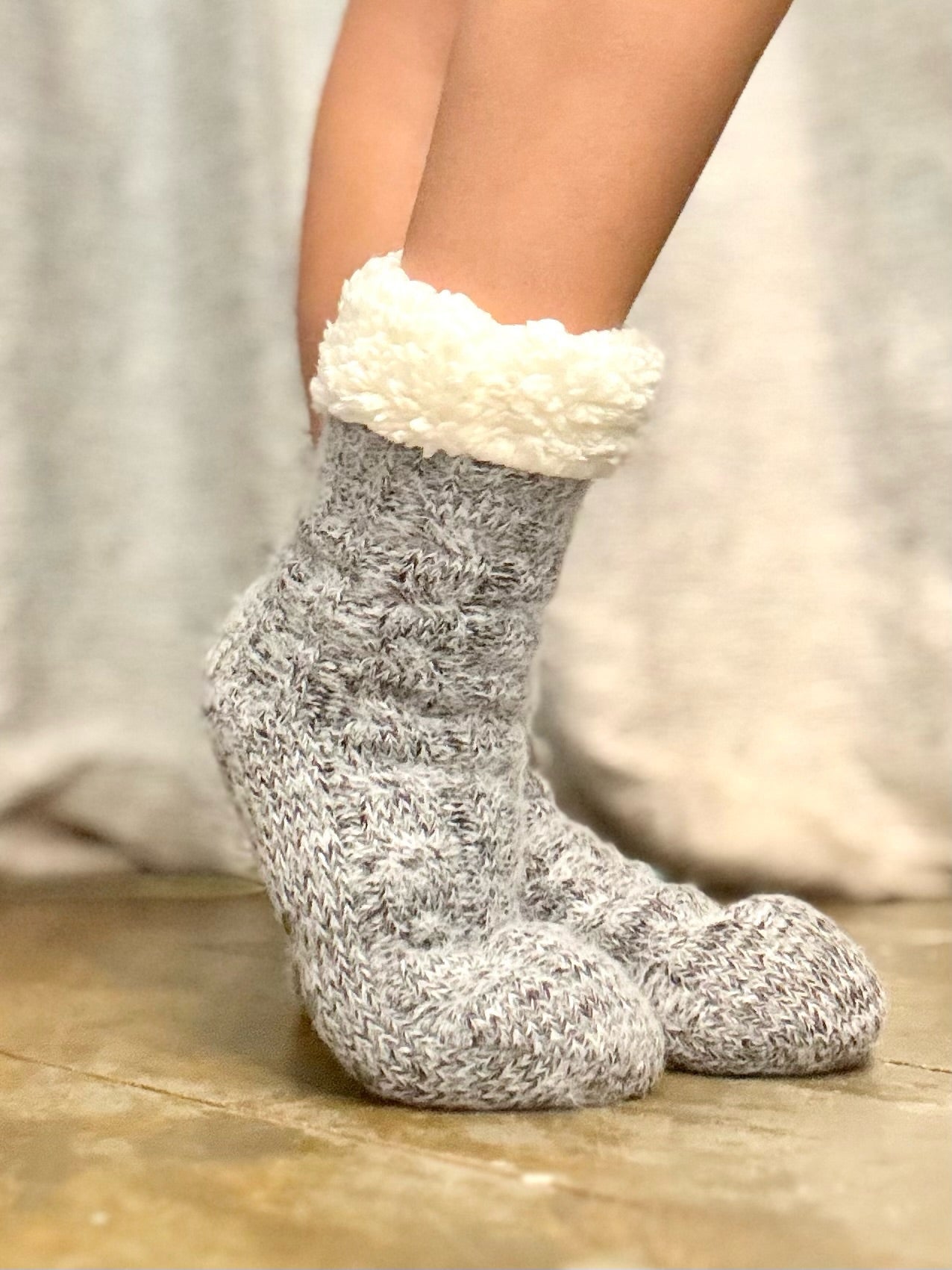 Gray socks with white cuffs worn by a person on a wooden floor.