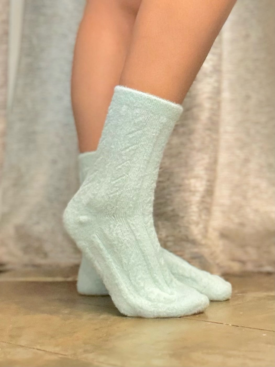 Light blue textured socks worn by a person on a wooden floor with a neutral background