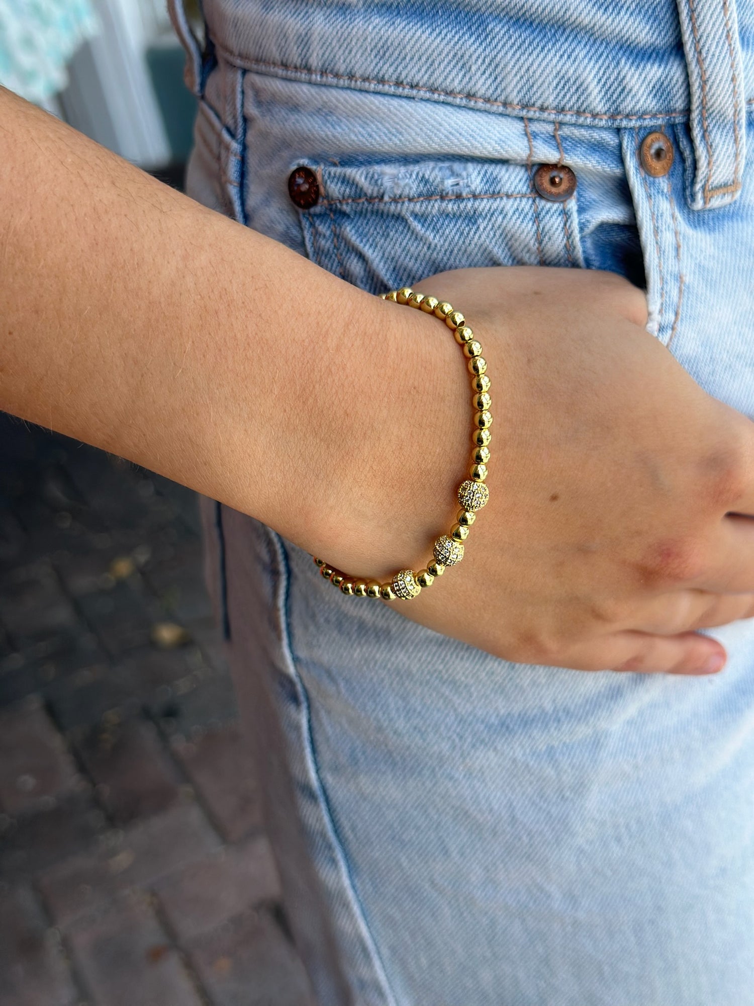 Gold bracelet on a wrist with light blue jeans in the background