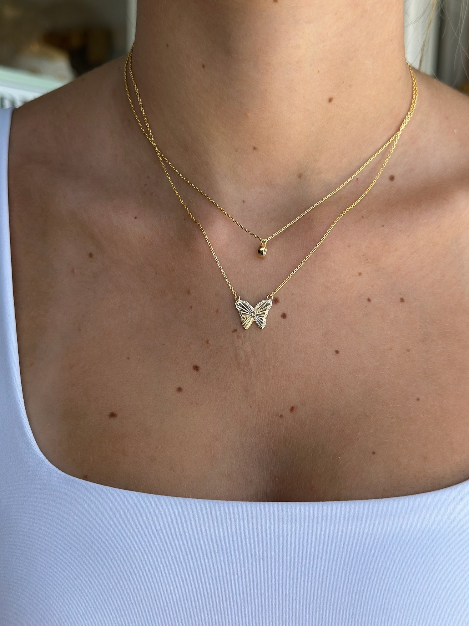 Gold butterfly necklace on a person wearing a white top