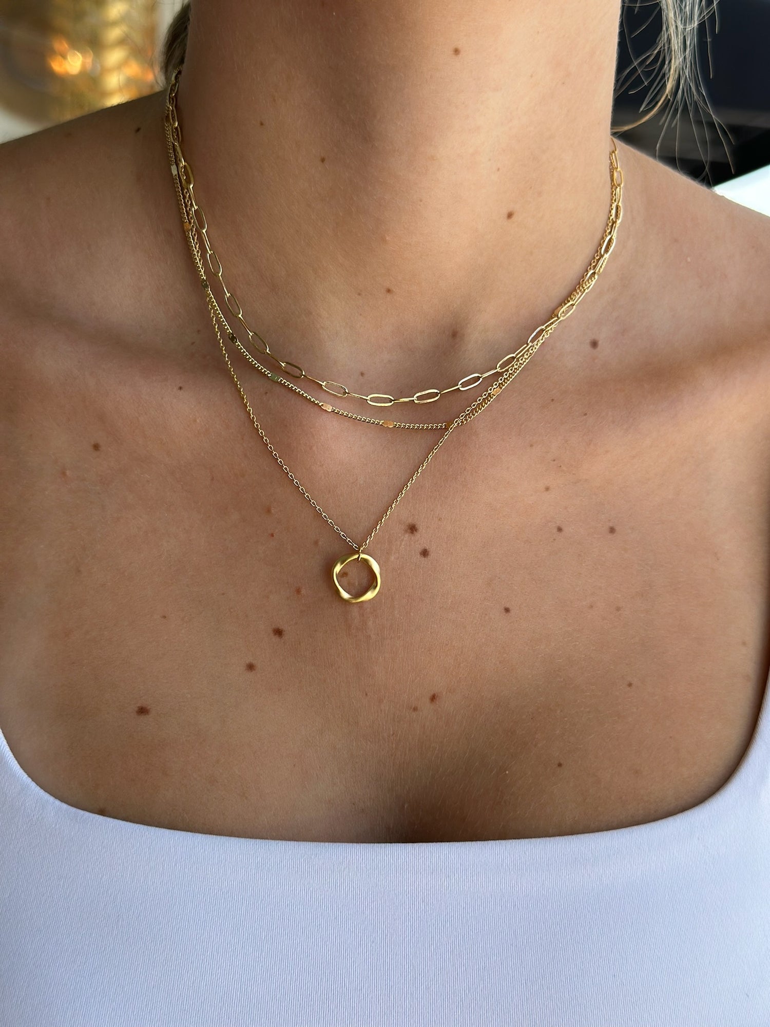 Close-up of a person wearing two gold necklaces on a plain background