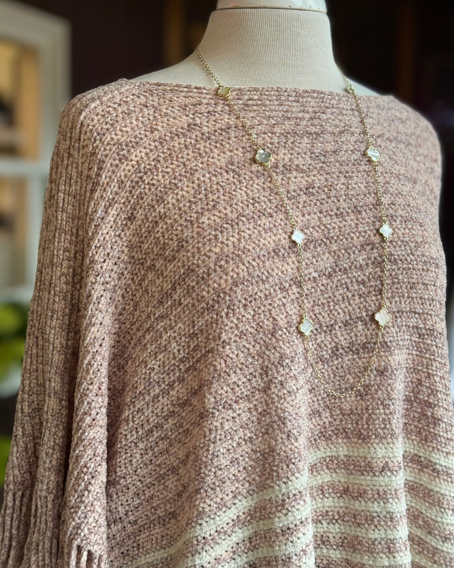 Mannequin wearing a brown knitted sweater with a long necklace.